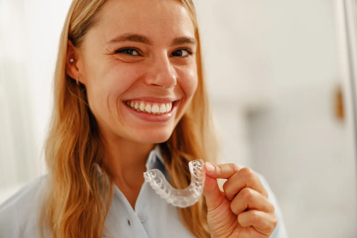 Young woman holding a clear aligner tray and smiling